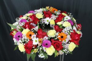 Corona de condolencias posición horizontal, floraciones multicolor con rosas rojas